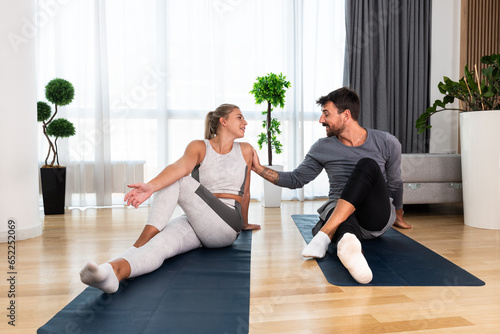 Couple exercising together. Man and woman in sportswear doing workout at home. Partners doing yoga class in the apartment on yoga mats stretching muscles breathing exercises after stress at work