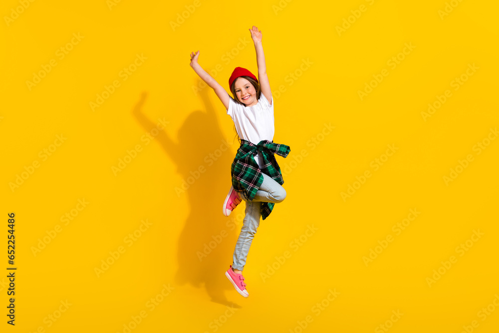 Full size photo of adorable schoolgirl raise hands jumping up wear trendy white outfit isolated on yellow color background