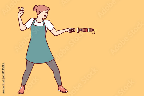 Housewife woman with vegetable kebab stands in swordsman pose and uses skewer instead of sword. Happy culinary girl in apron rejoices at opportunity to cook kebab from healthy ingredients