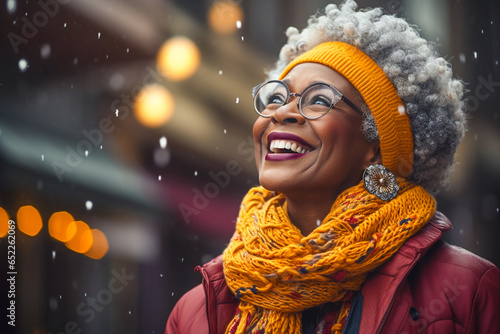 portrait of happy mature black woman with white hair looking up snowing in winter with scarf