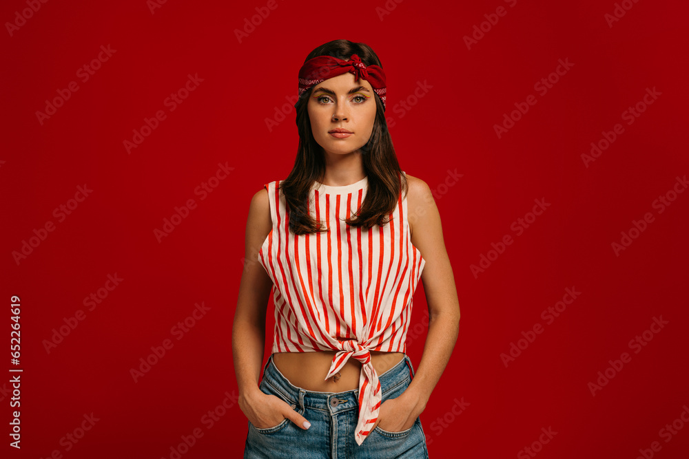 Stylish young hipster woman looking at camera while standing on red background