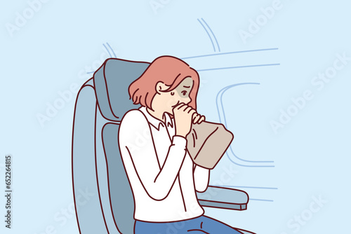 Woman passenger of airplane suffers from aerophobia and breathes into paper bag, sitting in airliner near porthole. Girl client of airline is stressed due to aerophobia or getting into turbulence zone