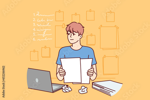 Man freelancer is doing paperwork, sitting at table with laptop and documents and thinking about plan for further actions. Guy does paperwork and makes list or checklist of future tasks