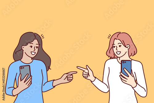 Women with mobile phones point fingers at each other, rejoicing at first meeting after acquaintance in social networks. Happy girls with phones, advertise applications for communication photo