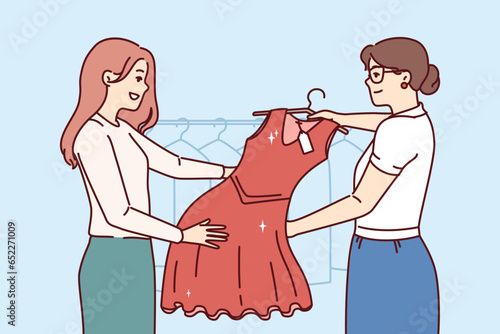 Woman picks up dry-cleaner dress standing in laundry room next to employee demonstrating cleaned clothes. Happy girl visitor to boutique, buys red evening dress for going to party.