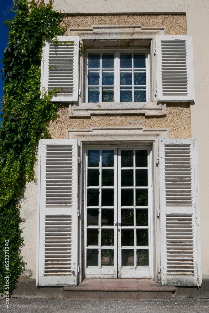Vertical shot of a wooden door and window with an open white shutters