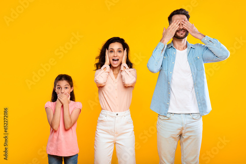 Hear no evil, see no evil, speak no evil. Family of three people covering eyes, ears and mouth, yellow background