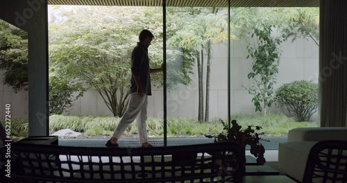 Man open glass sliding door at contemporary vacation home. Luxury apartment with minimalist style, modern furniture and panoramic window with backyard view.