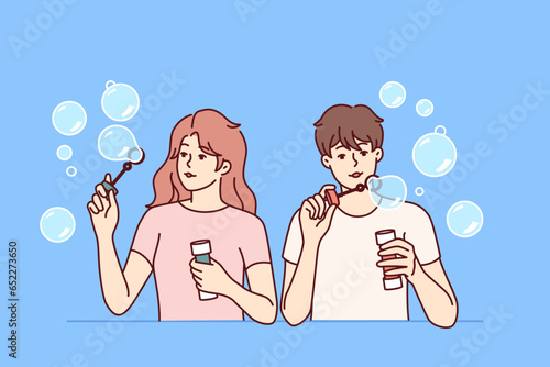 Man and woman inflate soap bubbles and have fun in free time, enjoying pastime together. Couple of casual teenagers with soap bubbles in hands playing and refusing to do useful things