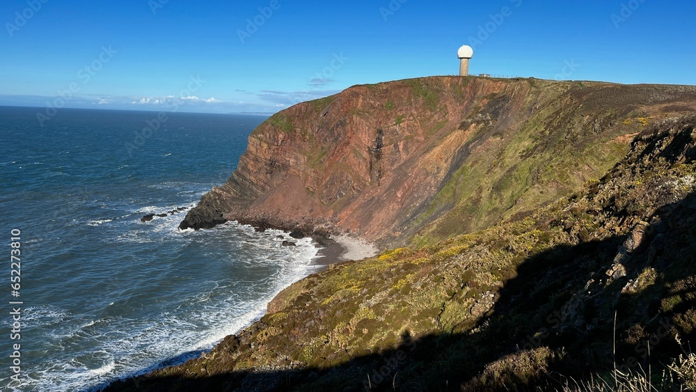 Lighthouse perched atop a steep cliff overlooking the expansive ocean waves below in Cornwall.