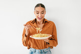 Excited young lady holding plate and enjoying tasty spaghetti, standing over white studio background wall