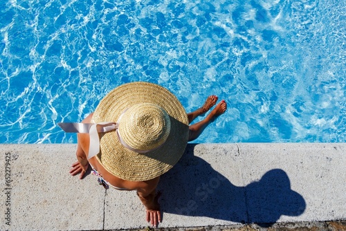Person wearing a stylish hat sitting next to a bright blue swimming pool