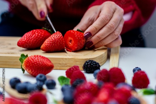 Φωτογραφία Female slicing strawberries with a kitchen knife in front of fresh strawberries
