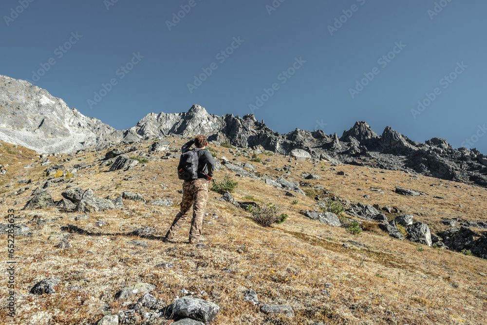 A male tourist with a backpack climbs uphill to a rocky peak. The concept of motivation and achieving your goals