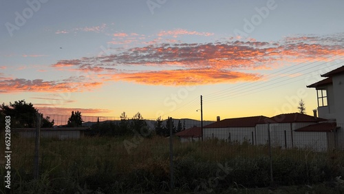 the sunset reflecting off of the sky over a field in front of some houses