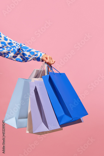 Sale offer. Black Friday. Shopping discount. Closeup of lady's hand holding purchase blue bags isolated on pink empty space background.