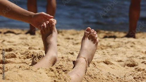 Child, tickling sibling on the beach on the feet with feather, kid cover in sand, smiling, laughing, enjoying some fun