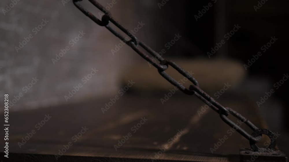 Close-up of a dark metal chain from a wooden bed in an old prison cell. A dark room with a massive wooden bed hanging on chains. The old prison. Close-up of a dark metal chain from a wooden bed in an old prison cell. A dark room with a massive wooden bed hanging on chains. The old prison.
