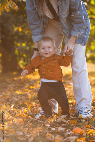 Portrait of a little boy 9 months old in the open air. A happy child in an autumn park takes his first steps. The guy is wearing a bright orange sweater. Happy childhood and motherhood.