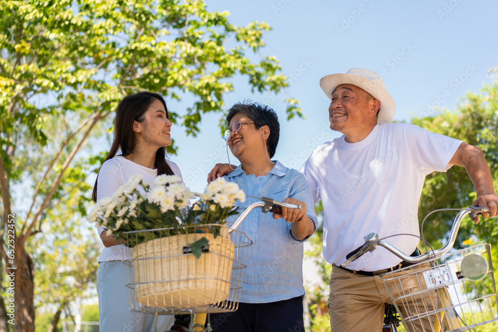 Obraz premium Happy and healthy Asian family standing beside a bicycle after workout together. friendship lifestyle, Enjoyment of active seniors, outdoor activity after retirement, health care insurance concept.