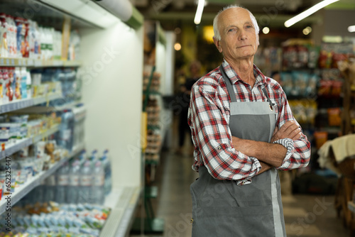 Canvas Print Confident smiling elderly supermarket clerk posing at the shopping mall, looking to the camera