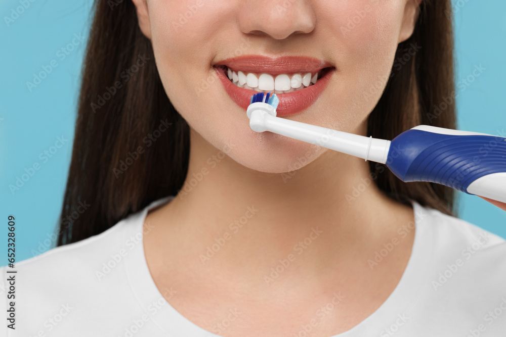 Woman brushing her teeth with electric toothbrush on light blue background, closeup Woman brushing her teeth with electric toothbrush on light blue background, closeup