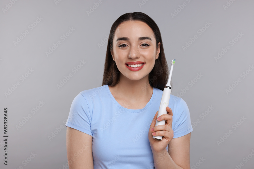 Happy young woman holding electric toothbrush on light grey background Happy young woman holding electric toothbrush on light grey background