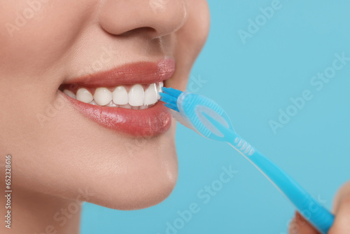 Woman brushing her teeth with plastic toothbrush on light blue background, closeup