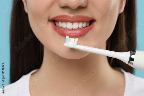Woman brushing her teeth with electric toothbrush on light blue background, closeup