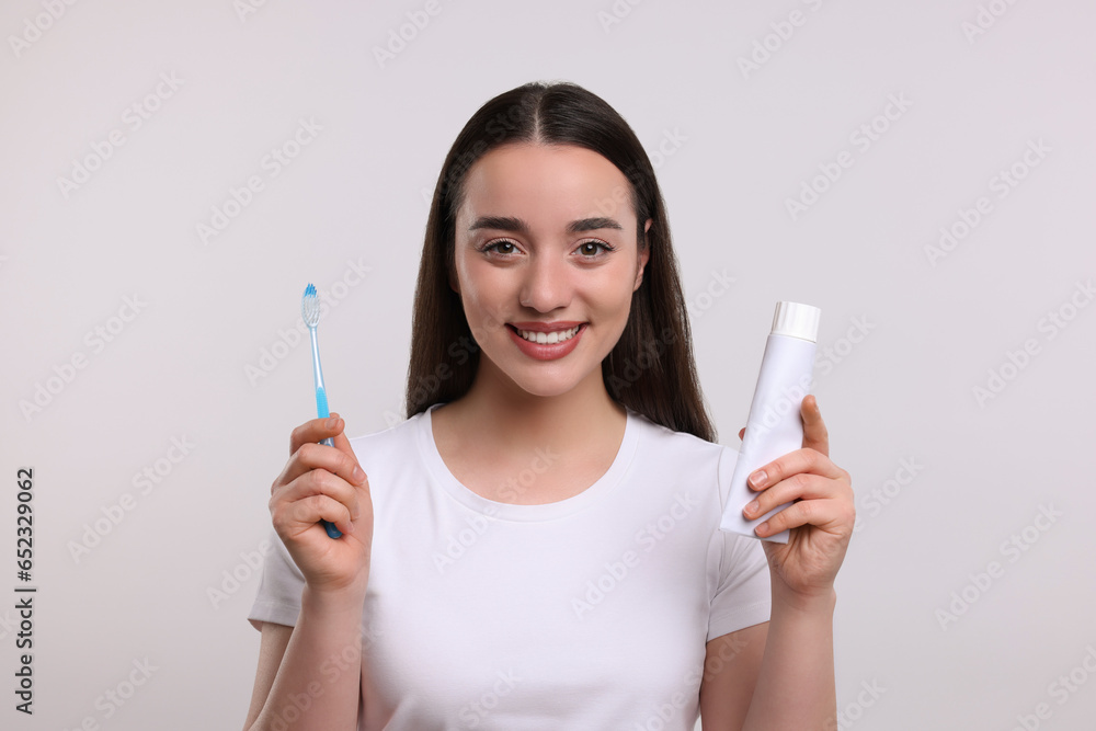Happy woman holding plastic toothbrush and tube of toothpaste on white background Happy woman holding plastic toothbrush and tube of toothpaste on white background