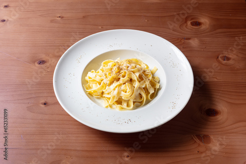 fettuccine, cacio, e, pepe, pecorino, romano, formaggio, dop, stagionato, 24, mesi, nero, di, maricha, pasta, italia, legno, tavolo, grezzo, venature, marrone, piatto, bianco, inclinato, prospettiva,  photo