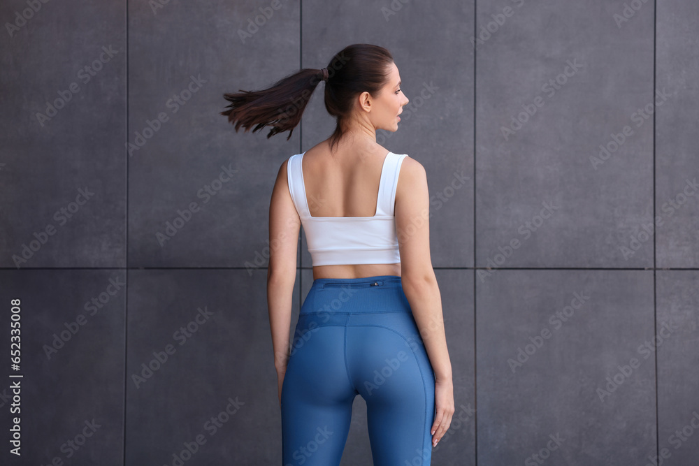 Woman in sportswear near dark grey wall, back view Woman in sportswear near dark grey wall, back view