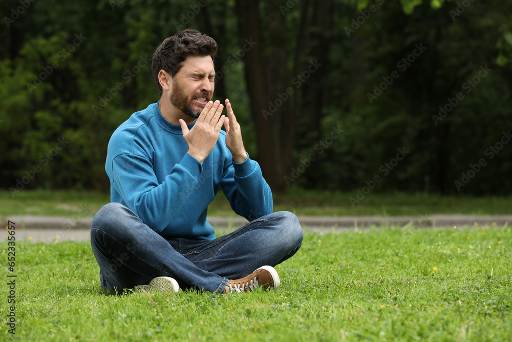 Man suffering from seasonal spring allergy on green grass in park. Space for text Man suffering from seasonal spring allergy on green grass in park. Space for text