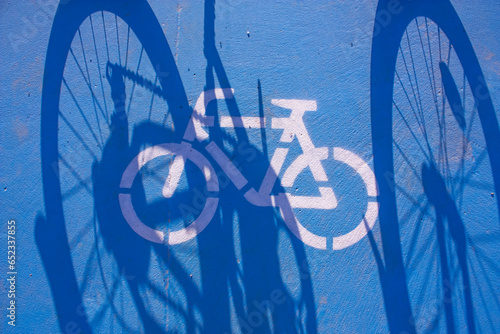 Blue bicycle path, shadow of bicycle and bicycle sign. Photograph.