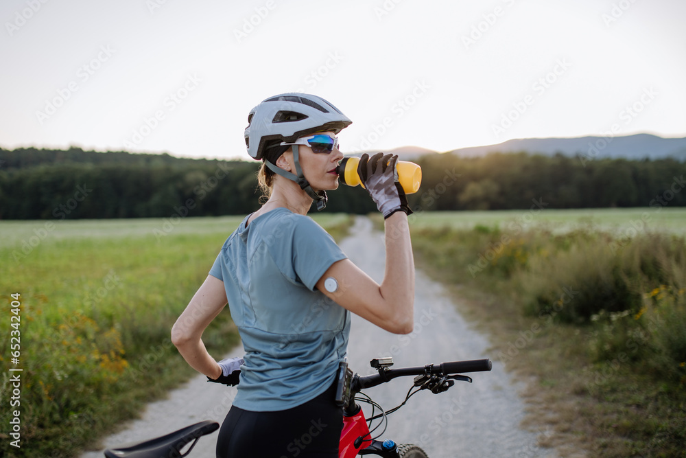 © Halfpoint - Diabetic cyclist with a continuous glucose monitor on her arm drinking water during her bike tour. © Halfpoint - Diabetic cyclist with a continuous glucose monitor on her arm drinking water during her bike tour.