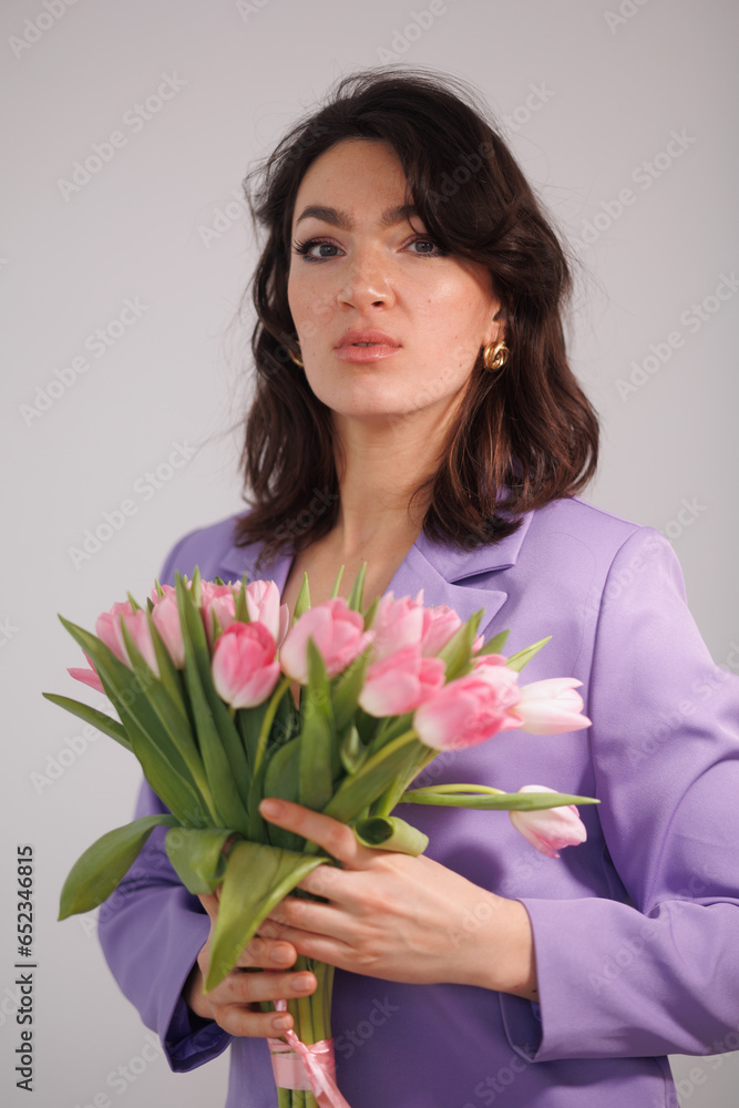 Beautiful brunette woman in violet costume with bucket of tulips, flowers, sitting on high chair. Girl smile, happy. Portrait of young office manage. Smile and freshness Beautiful brunette woman in violet costume with bucket of tulips, flowers, sitting on high chair. Girl smile, happy. Portrait of young office manage. Smile and freshness