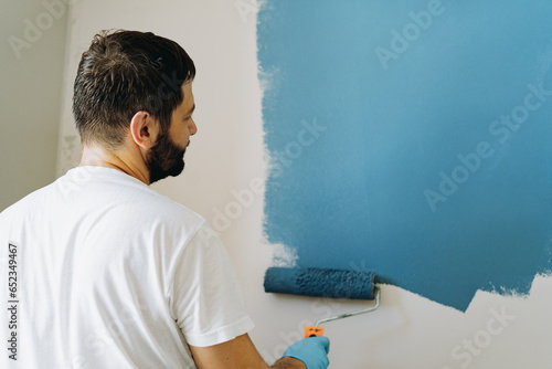 caucasian bearded man painting wall with paint roller. Painting apartment, renovating home