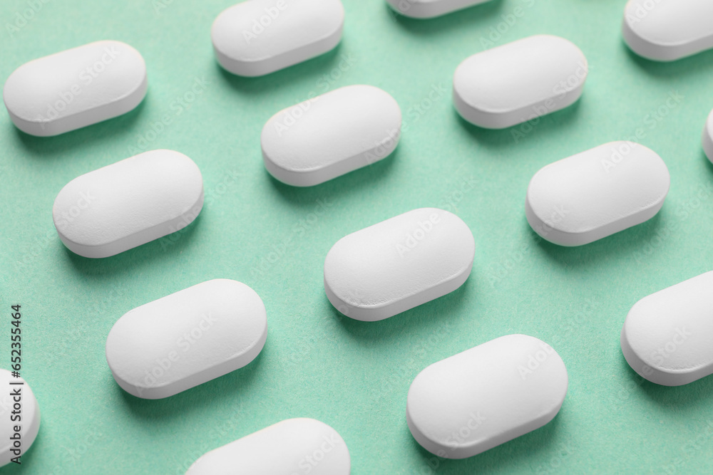 Many white pills on green background, closeup Many white pills on green background, closeup
