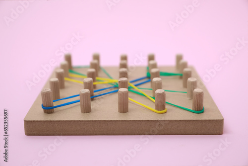Wooden geoboard with dragonfly shape made of rubber bands on pink background  closeup. Educational toy for motor skills development