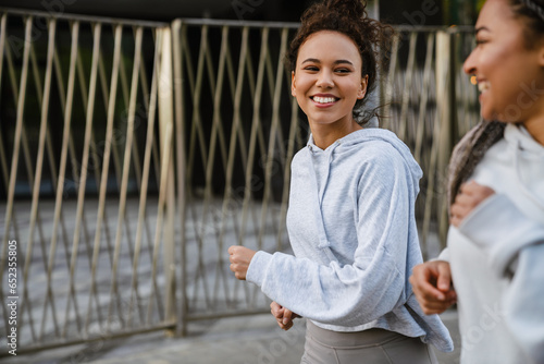 Two smiling fitness women running along city street