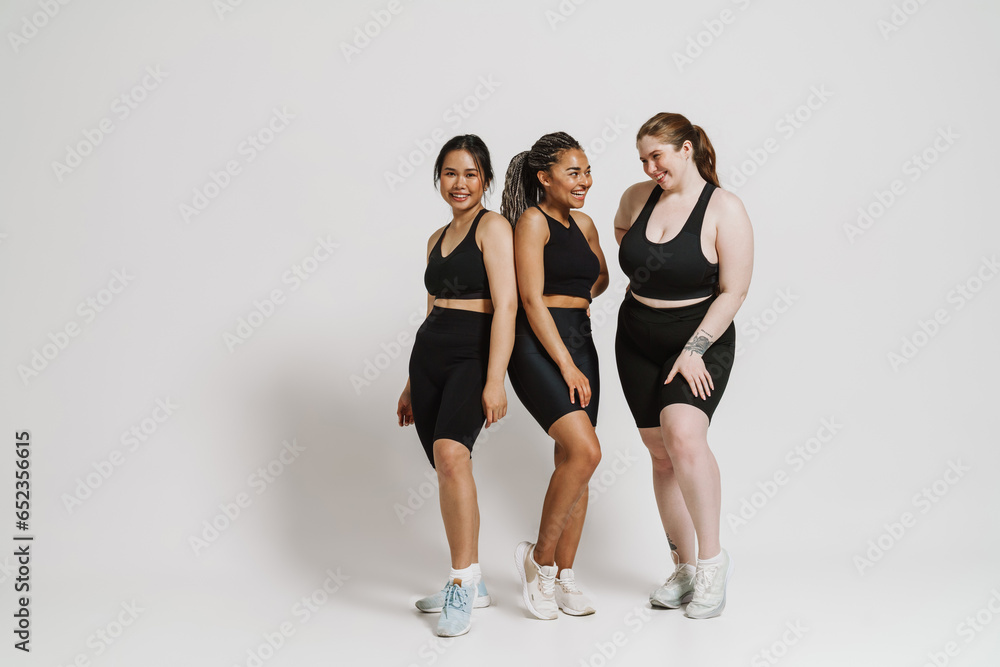 Group of smiling women in sportswear posing isolated over white wall Group of smiling women in sportswear posing isolated over white wall