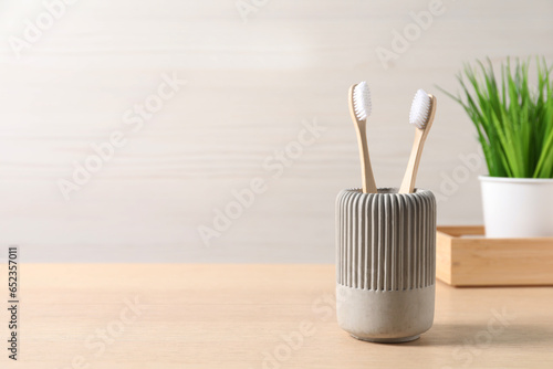 Bamboo toothbrushes in holder on wooden table, space for text
