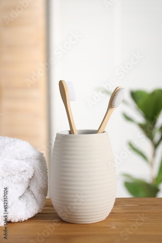 Holder with bamboo toothbrushes and towel on wooden table in bathroom