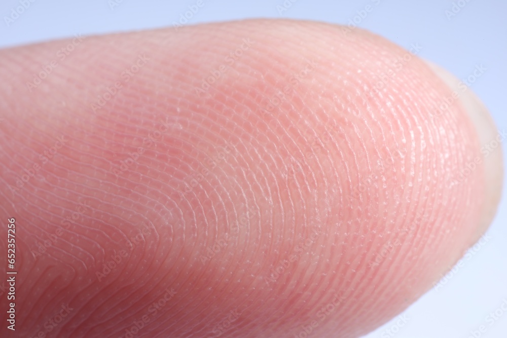Finger with friction ridges on light blue background, macro view Finger with friction ridges on light blue background, macro view