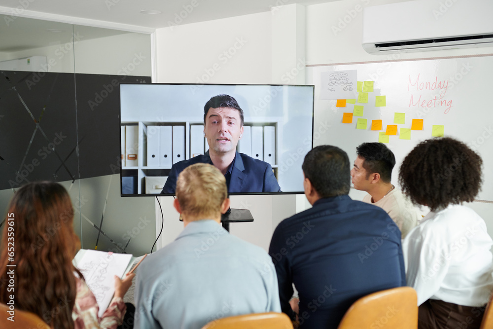 Fototapeta premium Team gathered in front of big screen to listen to speech of company CEO