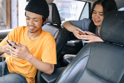 Asian male taxi driver and woman passenger having transaction using smart phone in car