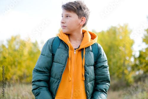 Portrait cheerful teen walking school at autumn. Boy is in yellow hood looking camera