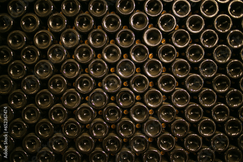 A stack of wine bottles in a wine cellar. The bottles are of different shapes and sizes, all arranged to make the image stand out. The bottles are all different colours and shapes,  photo