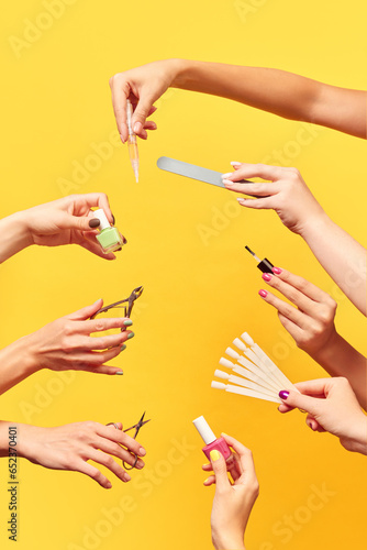 Female hands holding different tools for manicure against yellow background. Nail polish, cuticle oil, scissors, file. Manicure salon. Concept of hand care, cosmetics and cosmetology, spa, natural