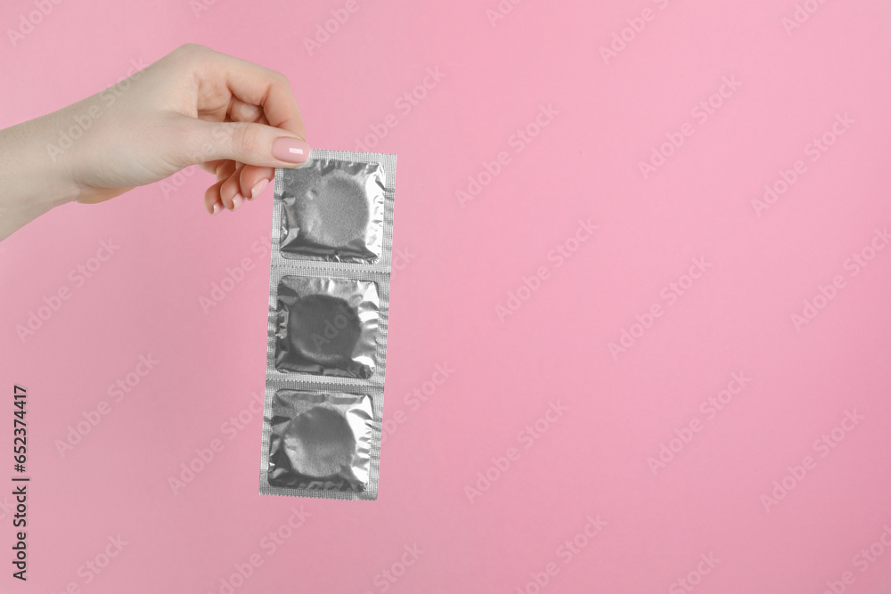 Woman holding condoms on pink background, closeup. Space for text